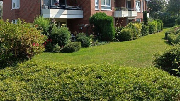 A two-story residential building with a red-tiled roof, multiple balconies, and a well-maintained garden. - Bupa06210 - Fewo "passat Söss-teihn" (Fehmarn)