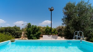 Una piscina rectangular con una superficie de agua azul cristalina, rodeada de abundante vegetación y un farol alto.