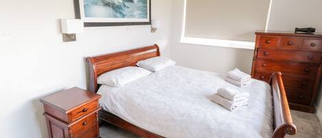 Un dormitorio ordenado con una cama de madera, una mesita de noche, un aparador y un cuadro en la pared.