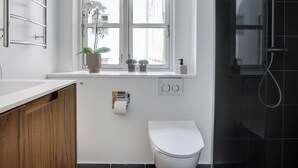 A bathroom with a white toilet, a window with a potted plant, and a shower area. - Regent 1 - Lovely 2-bdr Apt w Terrace (Copenhagen)