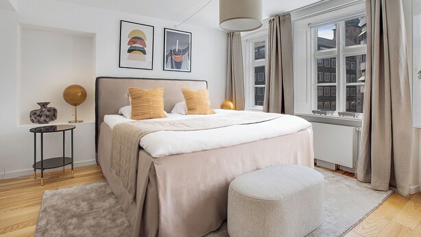 A modern bedroom with a large bed, a bedside table, a lamp, and a window with curtains. - Regent 1 - Lovely 2-bdr Apt w Terrace (Copenhagen)
