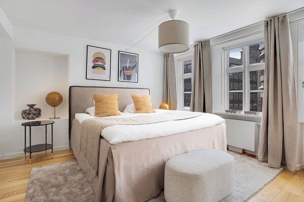 A modern bedroom with a large bed, a bedside table, a lamp, and a window with curtains.