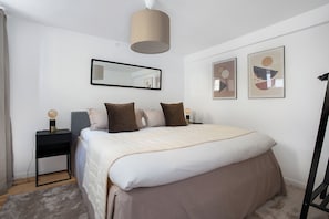 A bedroom with a bed, a nightstand, a lamp, a mirror, and two framed pictures on the wall.