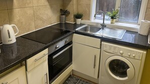 A compact kitchen with a built-in stove, oven, sink, and dishwasher. There is a window above the sink, and a small plant on the windowsill. - Marble Arch Family Apartments Posh Central London (London)