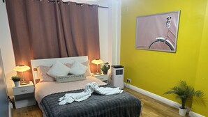 A neatly made bed with a dark bedspread and two pillows, a bedside lamp, a small potted plant, and a wall-mounted air purifier. - Marble Arch Family Apartments Posh Central London (London)