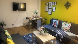 A modern living room with a dining area, a flat-screen TV mounted on the wall, and a vibrant yellow accent wall with framed pictures. - Marble Arch Family Apartments Posh Central London (London)