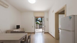 A kitchen with a refrigerator, a dining table with chairs, and a TV on a cabinet. - 1975 Villetta La Pineta 2 by Barbarhouse (Porto Cesareo)