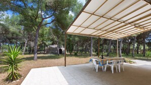 An outdoor patio area with a covered table and chairs, surrounded by trees and a stone wall. - 1975 Villetta La Pineta 2 by Barbarhouse (Porto Cesareo)