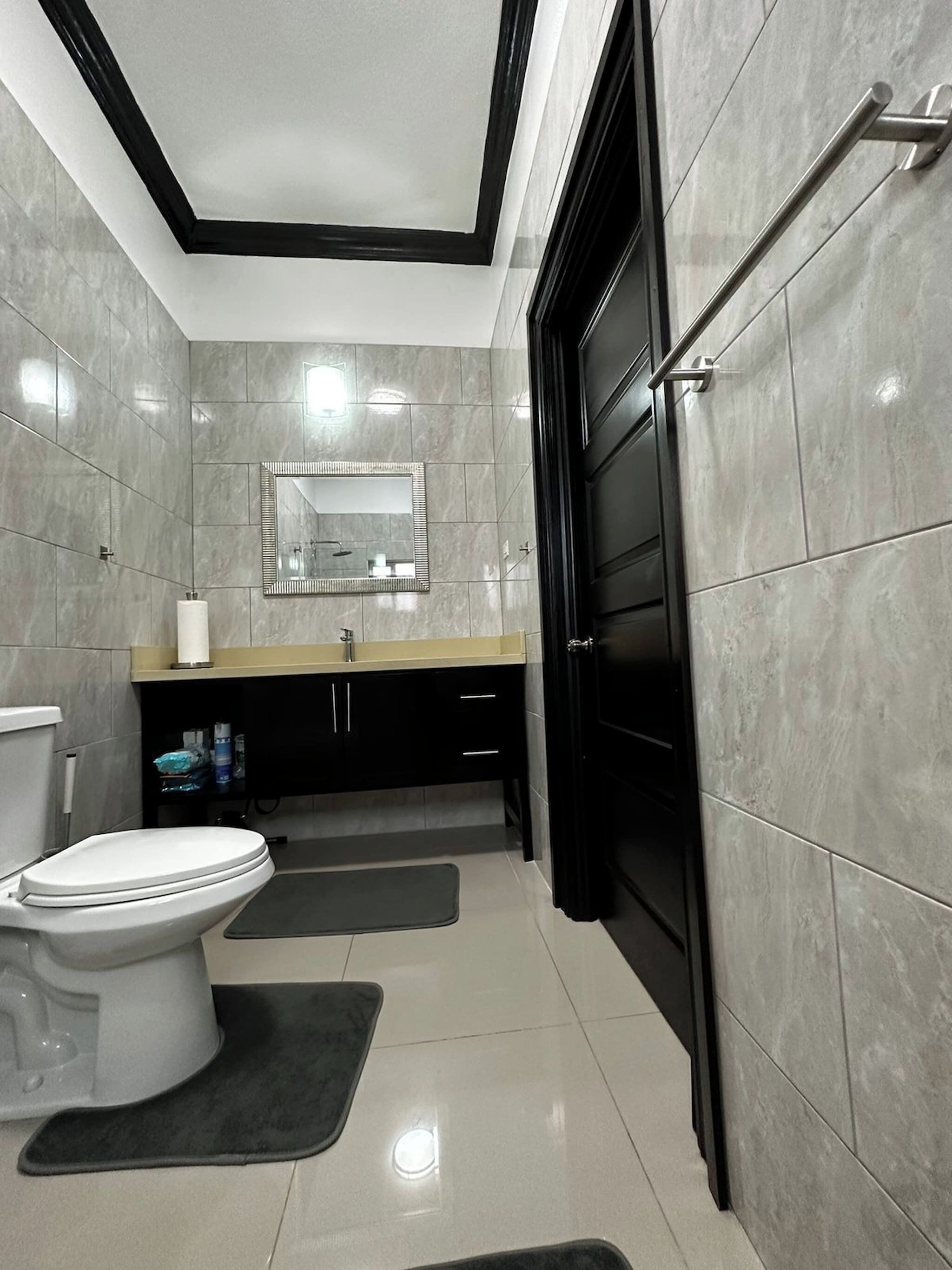 A modern bathroom with a toilet, sink, mirror, and black door.