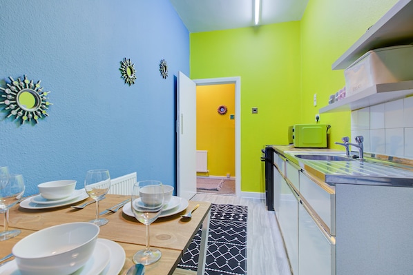 Une cuisine moderne avec une table à manger en bois pour quatre personnes, un réfrigérateur vert et un crédence carrelée blanche.