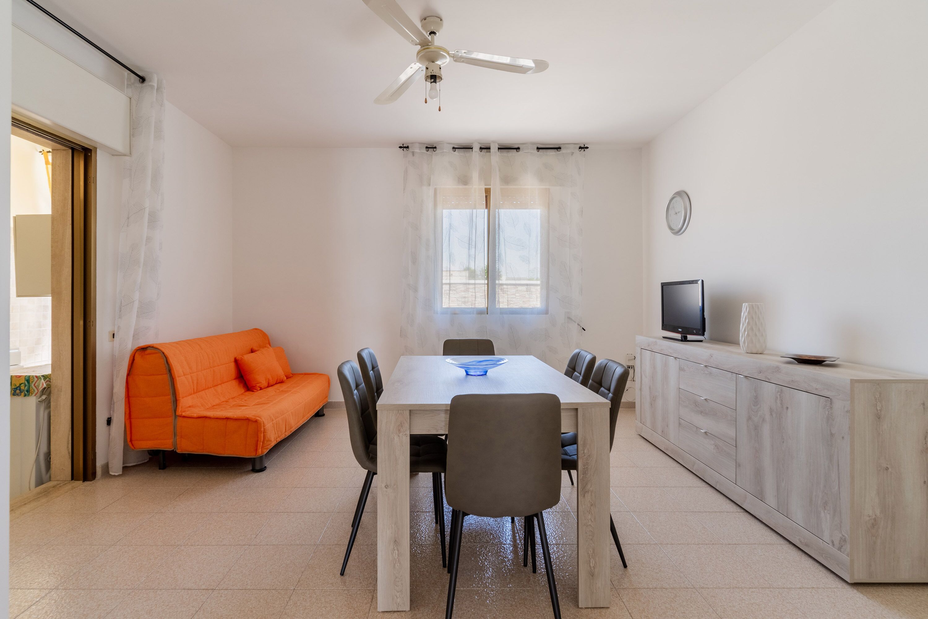 Un comedor con una mesa, sillas, un sofá, un televisor y un ventilador de techo.