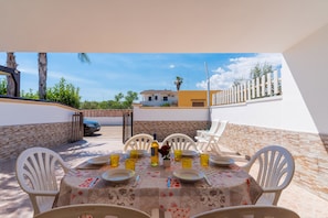 An outdoor dining area with a table set for six, surrounded by white chairs, a decorative tablecloth, and a view of a residential building in the background. - 3050 Villino Melissa by Barbarhouse (Porto Cesareo)