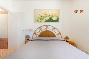 A bedroom with a bed, a wooden headboard, a nightstand, a lamp, and a painting of flowers on the wall. - 2960 Villetta Stella Mary - Bilo 2 by Barbarhouse (Nardò)