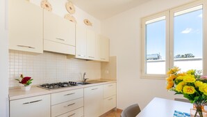 A kitchen with white cabinets, a gas stove, and a window with a view of buildings. - 2960 Villetta Stella Mary - Bilo 2 by Barbarhouse (Nardò)