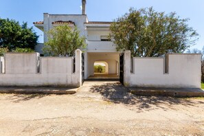 Un edificio con entrada central, rodeado de muros bajos y árboles, que conduce a un paseo cubierto.