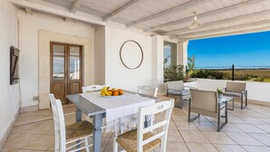 A covered patio with a dining table, chairs, and a view of the sea. - 3003 Masseria Surani Grande- Appartamento Sinistra by Barbarhouse (Manduria)