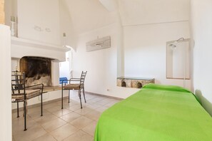 A room with a bed, a fireplace, a table with chairs, and a mirror on the wall. - 3003 Masseria Surani Grande- Appartamento Sinistra by Barbarhouse (Manduria)