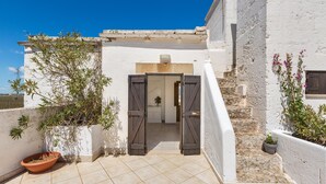 A white building with a tiled patio, a wooden door, and potted plants. - 3003 Masseria Surani Grande- Appartamento Sinistra by Barbarhouse (Manduria)