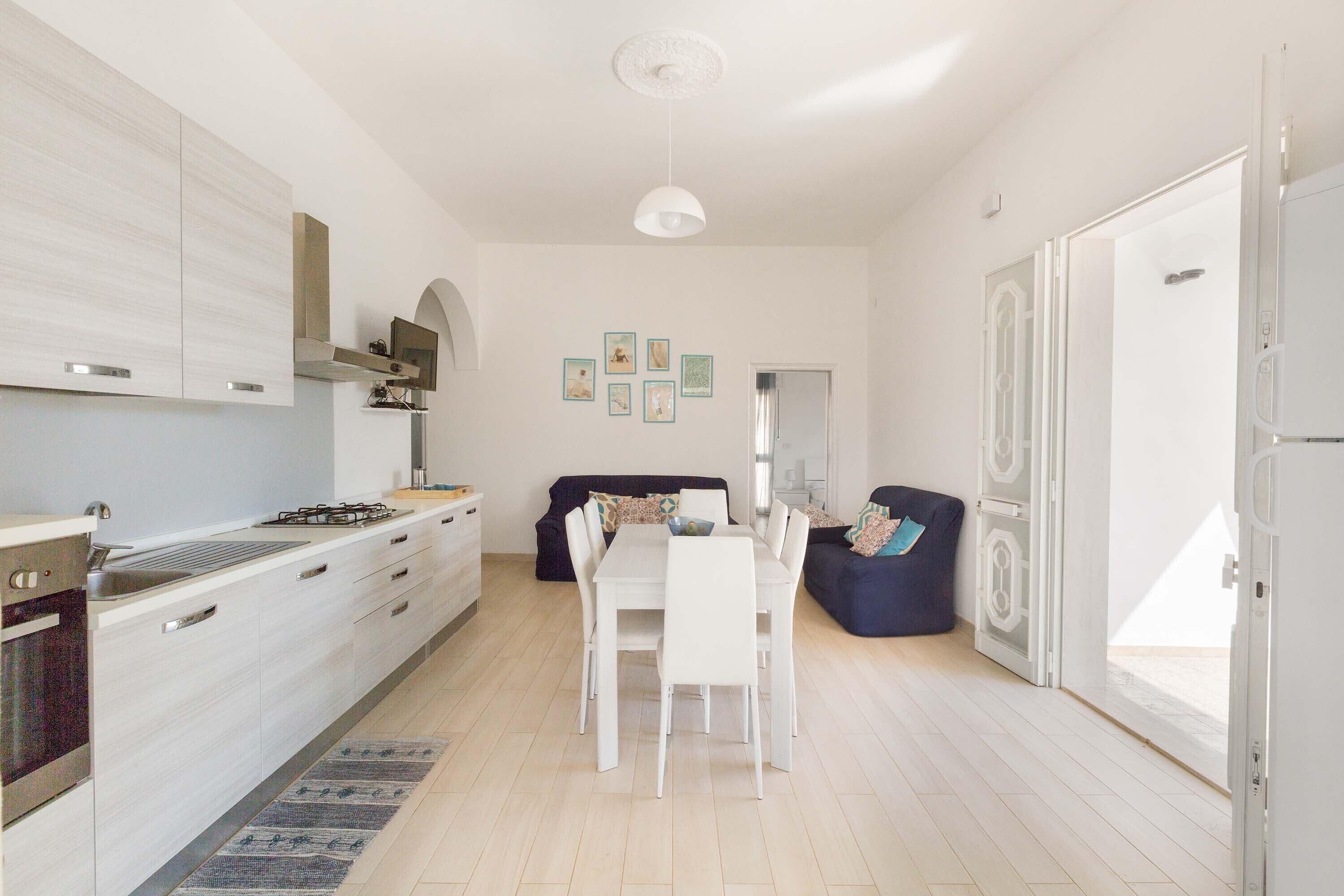 A modern kitchen with white cabinets, a dining table with chairs, and a blue sofa.