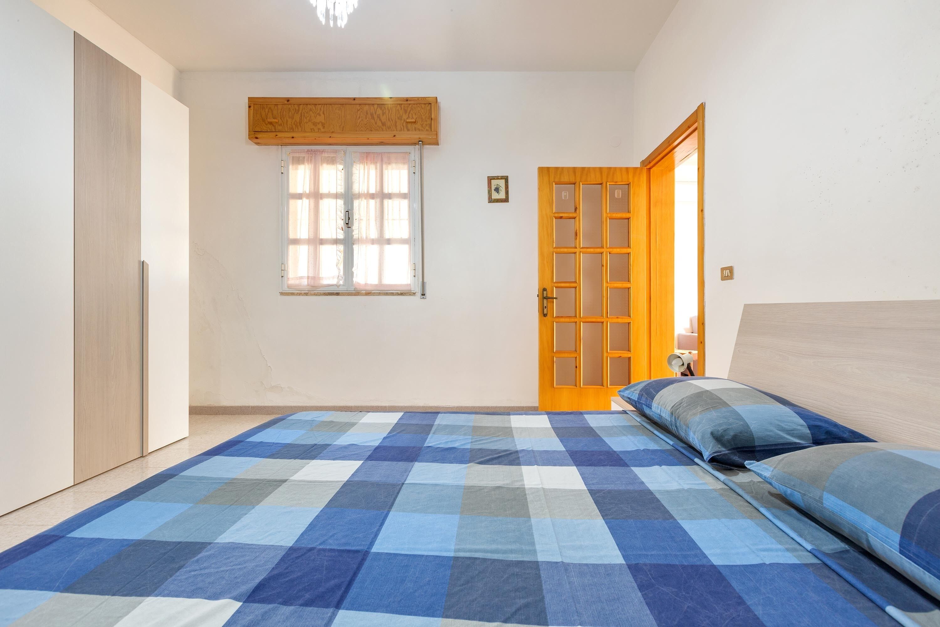 A bedroom with a checkered blue and white floor, a wooden door, and a window with curtains.