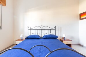 Un dormitorio con estructura de cama de metal, dos mesitas de noche con lámparas y una colcha azul.