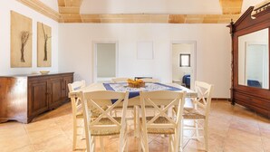 A dining area with a round table, white chairs, and a wooden cabinet. - 3002 Masseria Surani Grande- Appartamento Destra by Barbarhouse (Manduria)