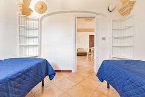 A room with two beds, white shelving units, and a doorway leading to another room.