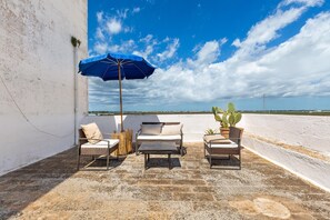 A patio with two wicker chairs, a table, and a blue umbrella.