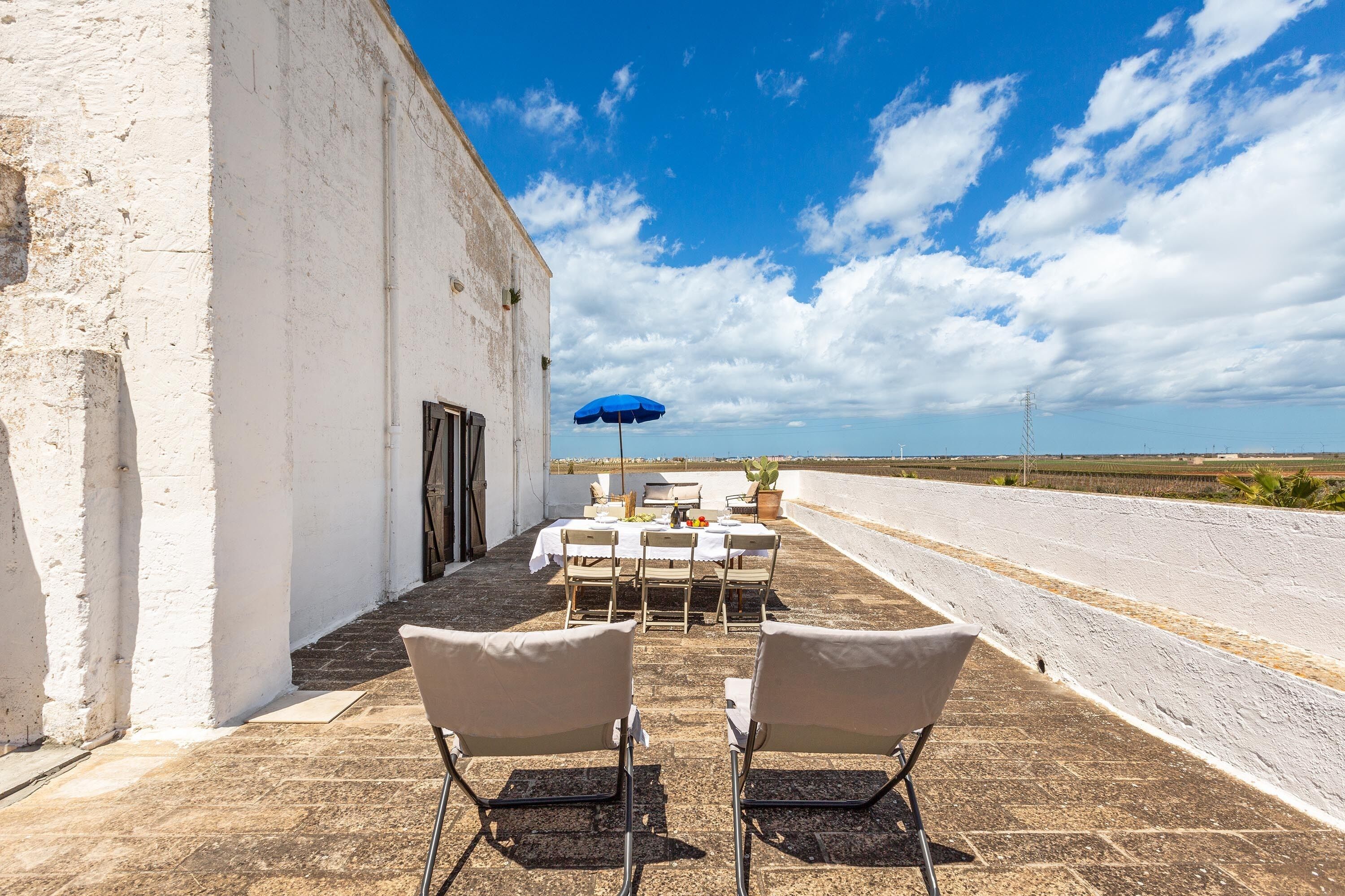 Eine Außenpatio mit Tisch und Stühlen, einem blauen Sonnenschirm und Blick auf das Meer.