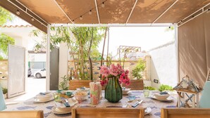 An outdoor dining area with a table set for two, surrounded by chairs, a vase with flowers, and a view of the street and buildings in the background. - 2473 Villetta Seaside by Barbarhouse (Porto Cesareo)