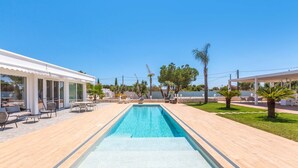 A swimming pool with a tiled deck, surrounded by outdoor seating and palm trees.