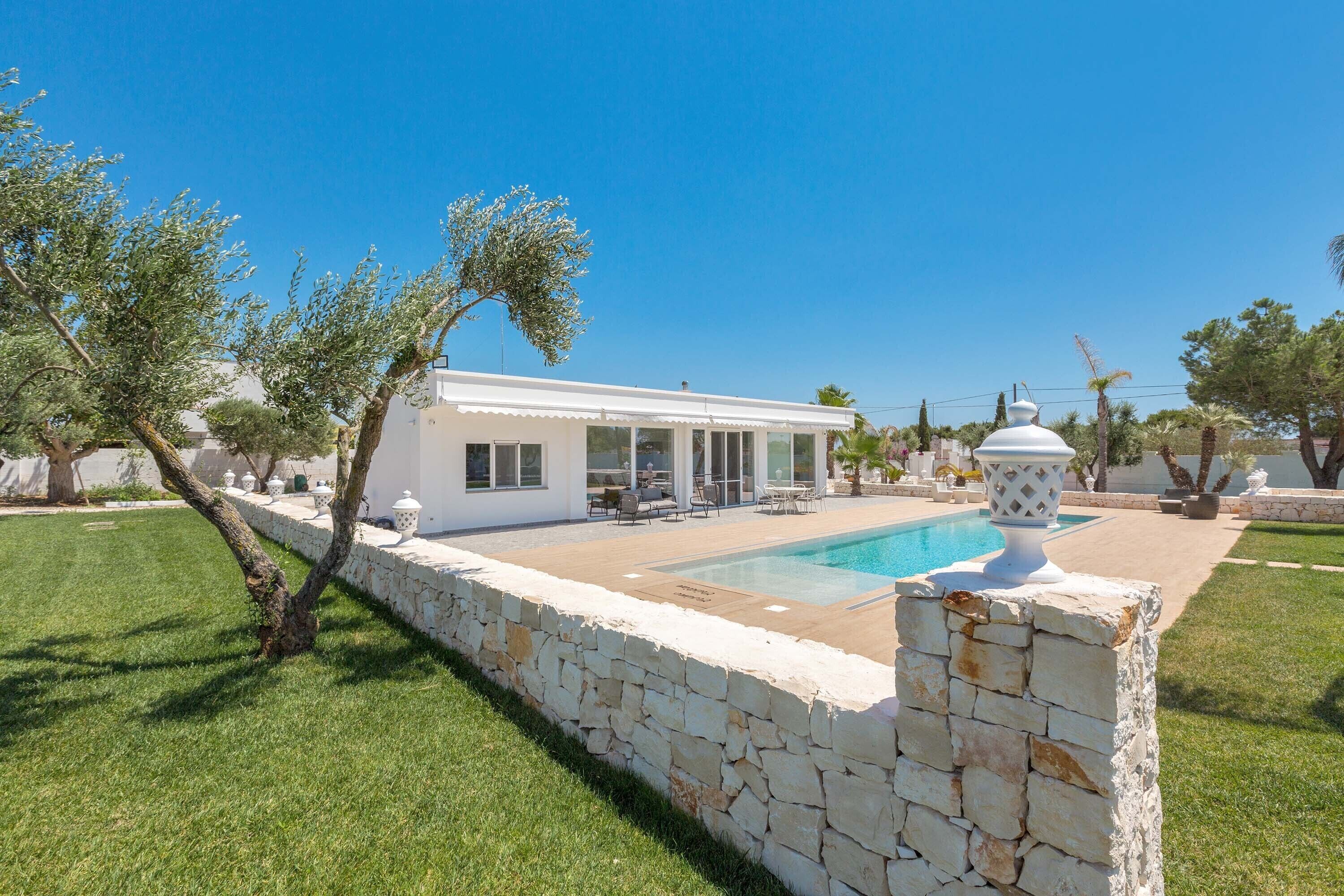Una casa moderna con piscina, muro de piedra y mobiliario exterior.