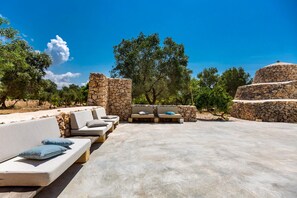 Zona salotto all'aperto con pareti in pietra e divani, immersa tra alberi e un cielo sereno.