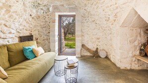A cozy room with a stone wall, a green sofa, a small round table, and a wooden shelf. - 2670 Trullo Corni di Fiasco by Barbarhouse (Maruggio)