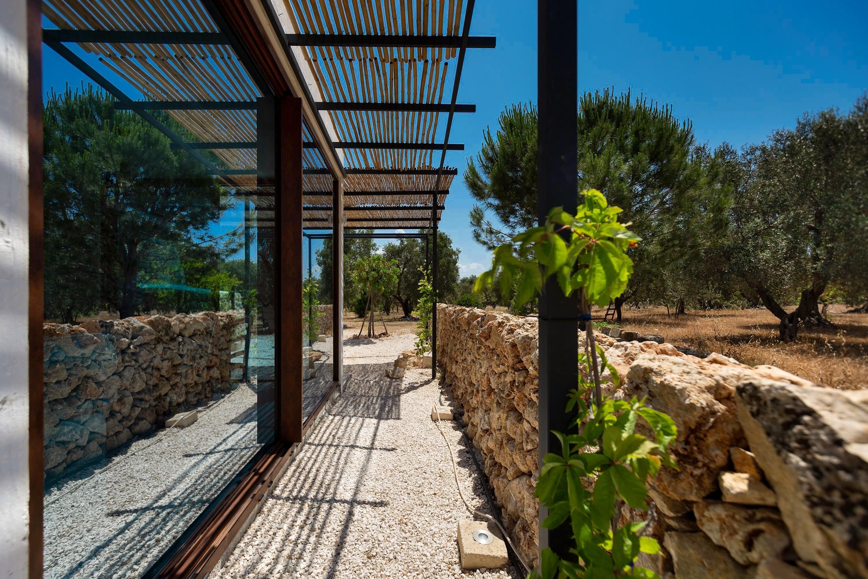 A modern outdoor area with a pergola, stone walls, and a gravel path.