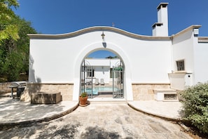 A white building with a large arched entrance, a swimming pool, and outdoor seating. - 1916 Villa Virgilia by Perle di Puglia (Martina Franca)