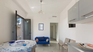 A compact living space with a dining table, a sofa, a kitchenette, and a door leading to an outdoor area. - 2127 Villa Ippocampo - Appartamento Rosso by Barbarhouse (Manduria)