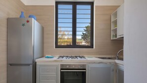 A compact kitchen with a built-in oven, a refrigerator, and a window with blinds. - 2127 Villa Ippocampo - Appartamento Rosso by Barbarhouse (Manduria)