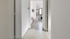 A hallway leading to a kitchen area with a chair and a table. - 2127 Villa Ippocampo - Appartamento Rosso by Barbarhouse (Manduria)