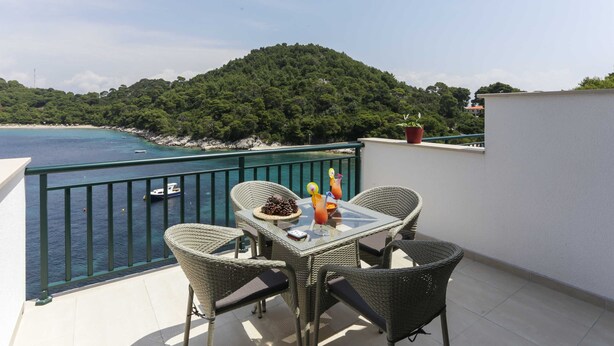 A balcony with wicker chairs, a glass table, and a potted plant. - Apartments Posta (Mljet)