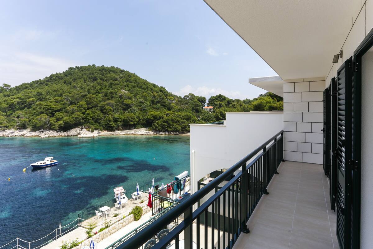 Ein Balkon mit Blick auf eine Küstenlandschaft, darunter ein Boot auf dem Wasser und ein Hügel mit Bäumen.
