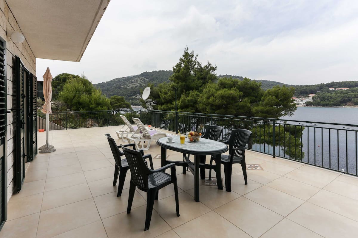 Eine Terrasse mit Tisch und Stühlen, eine Satellitenschüssel und Blick auf einen See und Hügel.