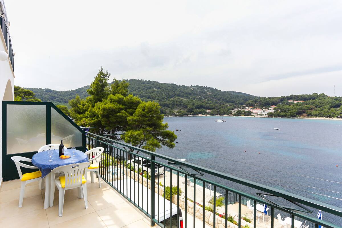 Ein Balkon mit Tisch und Stühlen, der auf ein Gewässer mit Booten und eine hügelige Landschaft im Hintergrund blickt.