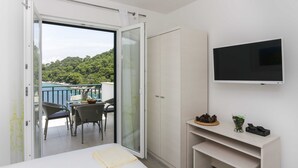A bedroom with a bed, a TV, a wardrobe, and a balcony with a table and chairs. - Apartments Posta (Mljet)