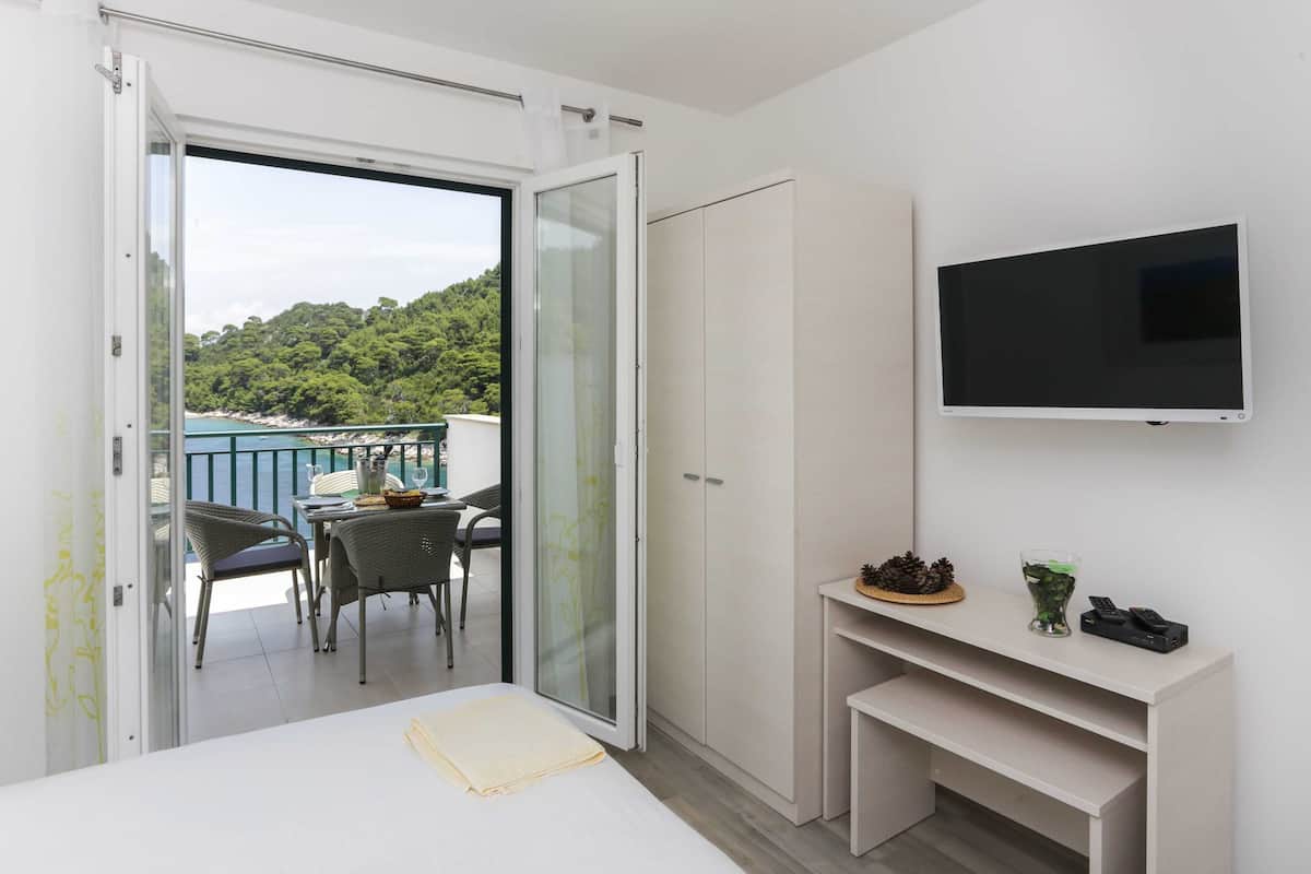 Ein Schlafzimmer mit Bett, Fernseher, Kleiderschrank und einem Balkon mit Tisch und Stühlen.