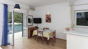 A room with a dining table, chairs, a TV, and a window overlooking a scenic view. - Apartments Posta (Mljet)