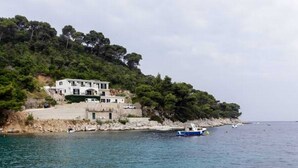 A coastal building with a stone base and upper floors, overlooking a calm sea with a small boat nearby. - Apartments Posta (Mljet)