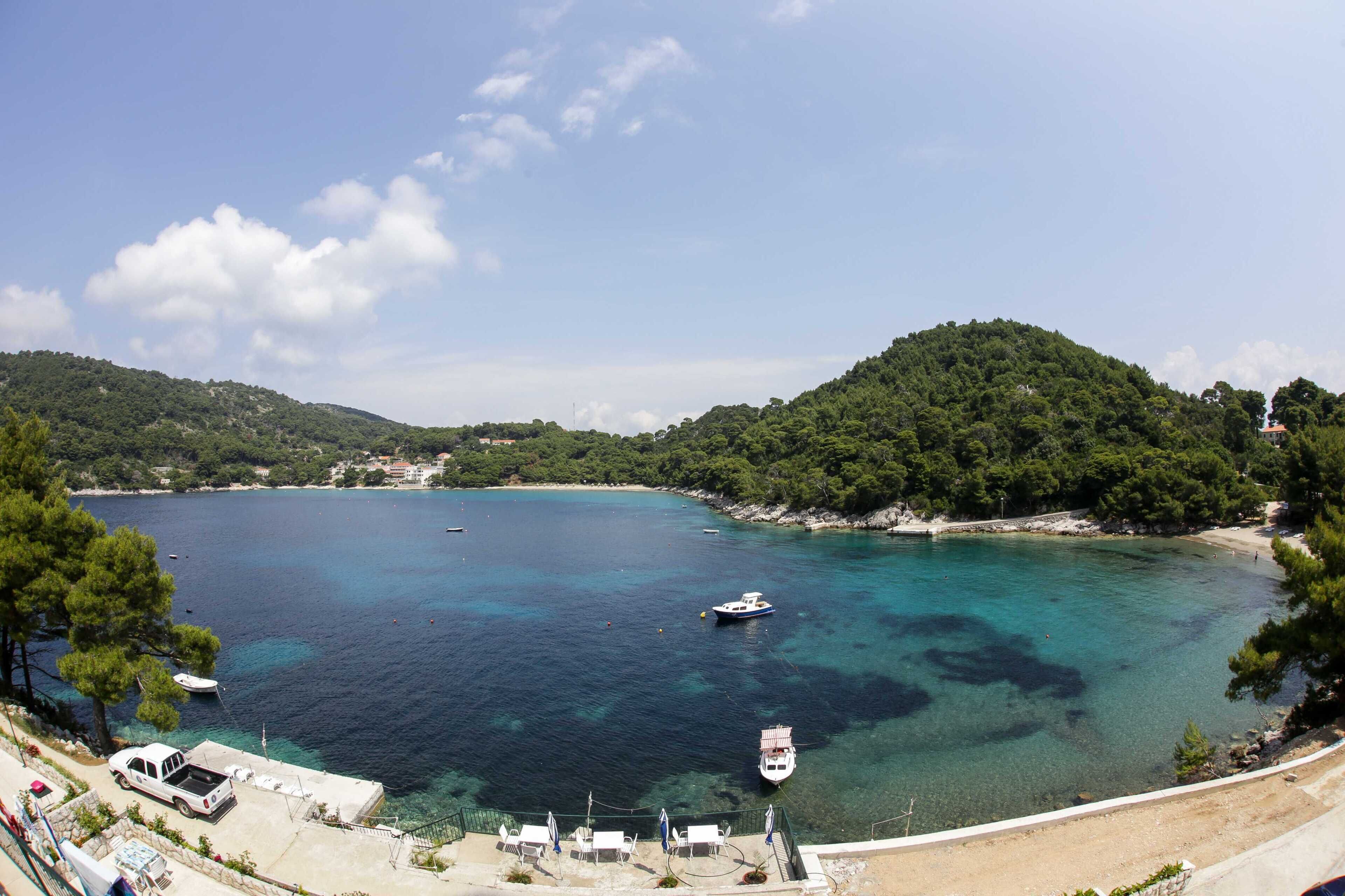 Vista costera con aguas turquesas cristalinas, barcos y una camioneta blanca estacionada cerca de la orilla.