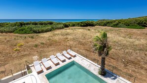 A pool area with lounge chairs and a view of the ocean.