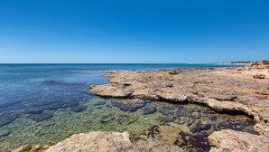 A rocky shoreline with clear water and a distant view of the sea.